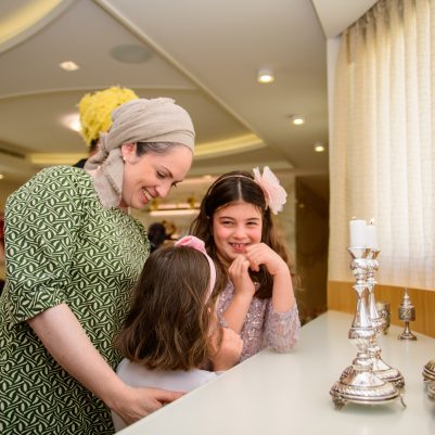 Mother and daughters smiling next to shabbat candles