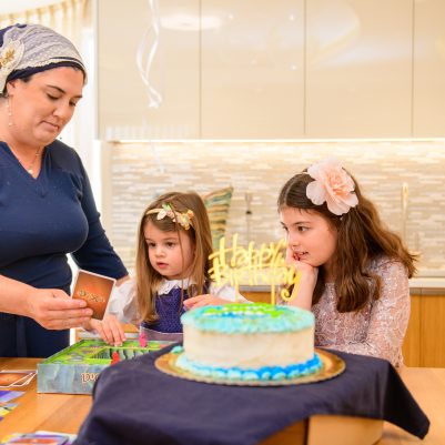 Mother and 2 daughters playing a board game, birthday cake on the table 2