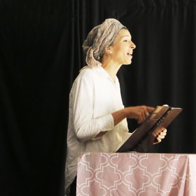 Woman teaching Torah to an audience while reading from the text