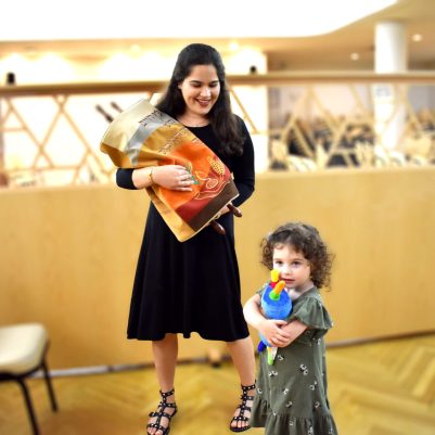 Young woman holding torah in shul next to little girl