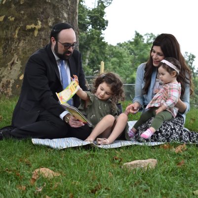 Family sitting on grass in park talking 1