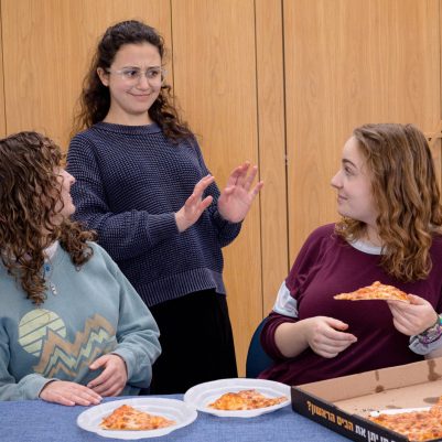 Two young women offering friend pizza 1