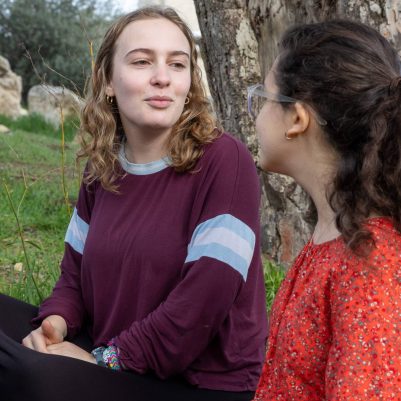 Two young women talking, sitting next to tree 1