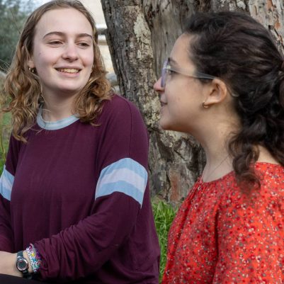 Two young women talking, sitting next to tree 2