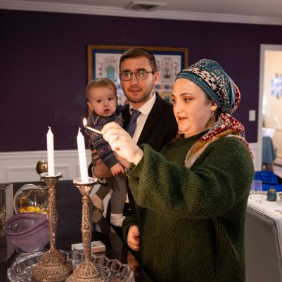 Woman lighting Shabbat candles next to family 1