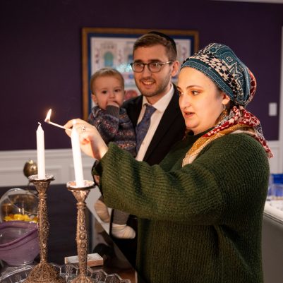 Woman lighting Shabbat candles next to family 2