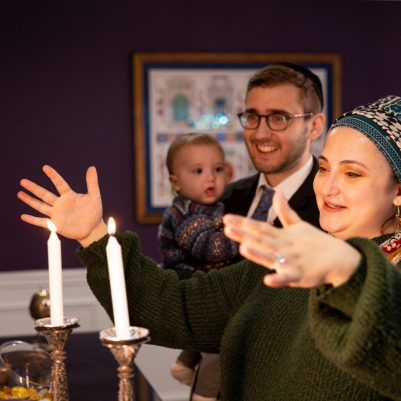 Woman lighting Shabbat candles next to family 3