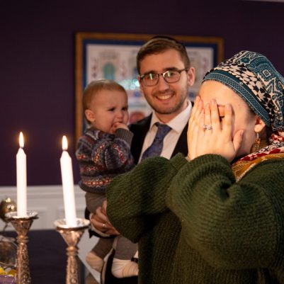 Woman lighting Shabbat candles next to family 4