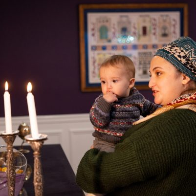 Woman holding baby looking at Shabbat candles 2
