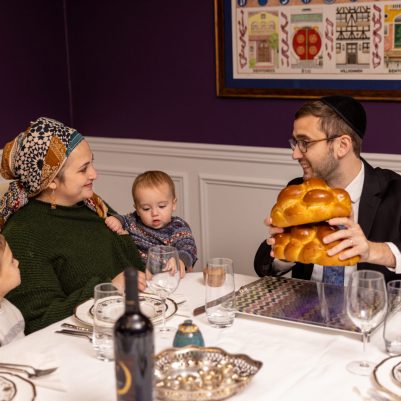 Father making Hamotzi at Shabbat table with family 1