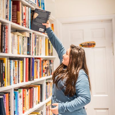 Young woman reaching for book on shelves 1