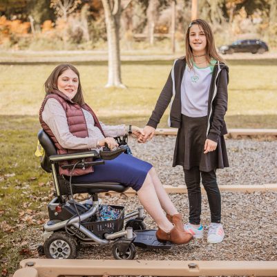 Woman in wheelchair and girl smiling at park