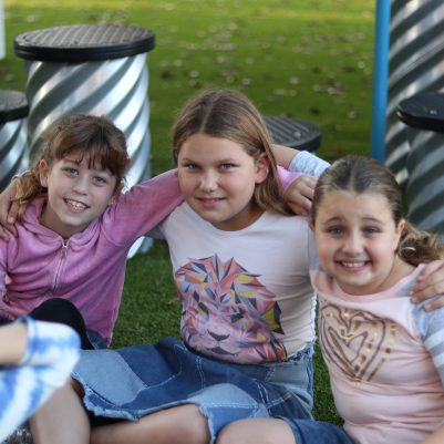 Happy Girls Smiling and Sitting on Grass Together in a Park Playground
