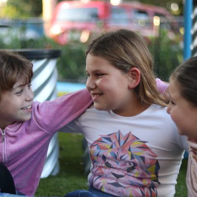 Group of Young Girls Sitting Close Together and Smiling During Outdoor Playtime