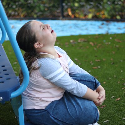 Young Girl Sitting on the Grass, Holding Her Knee in Pain