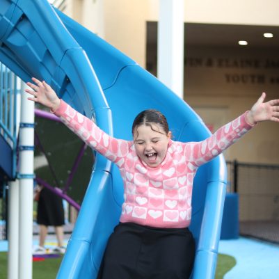 Smiling Young Girl Enjoying a Playground Slide with Arms Raised