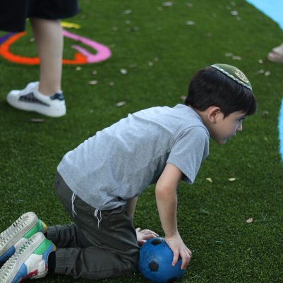Young Boy Kneeling on Grass and Holding a Ball at a Playground