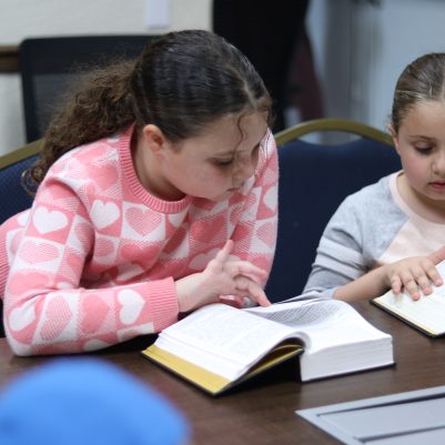 Two Young Girls Reading Books Together at a Table Indoors