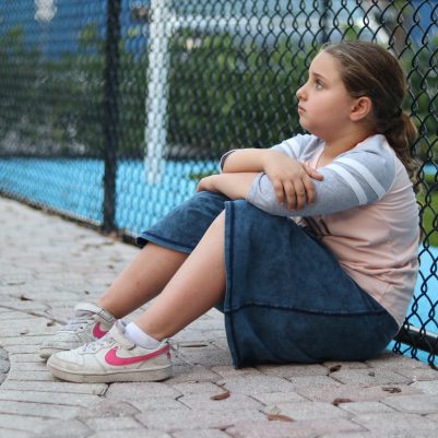 Young Girl Thinking and Sitting Alone at an Outdoor Playground