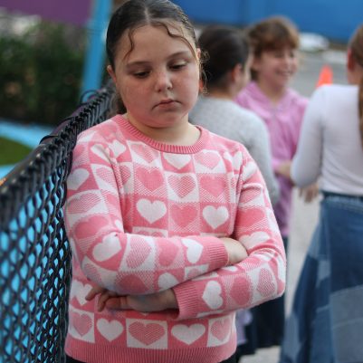 Sad Young Girl Standing Alone at a Playground While Other Children Play Nearby