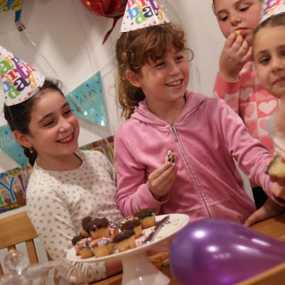 Group of Young Girls Celebrating a Birthday with Cupcakes and Party Hats Indoors