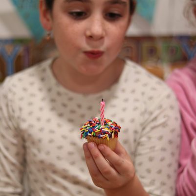Young Girl Wearing a Birthday Hat Blowing Out a Candle on a Cupcake