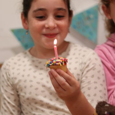 Young Birthday Girl Smiling and Holding a Sprinkle Cupcake with Candle
